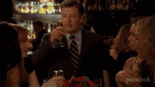 a man in a suit and tie is drinking from a glass at a bar .