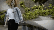 a woman wearing a denim jacket and a white t-shirt is walking down a street .