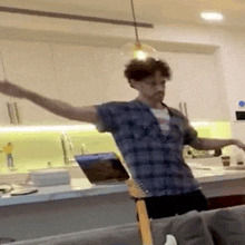 a man is standing in a kitchen with his arms outstretched while playing a guitar .
