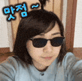 a woman wearing sunglasses has a bun in her hair and a foreign language written above her head
