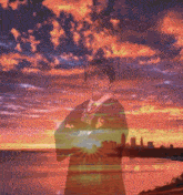 a boy in a suit and tie stands in front of a sunset over a body of water