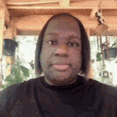 a man wearing a black shirt looks at the camera with a wind chime in the background