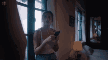 a woman in a white tank top holds a cell phone