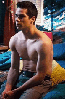a shirtless man is sitting on a bed in front of a window
