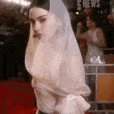 a woman in a white dress with a veil on her head is walking on a red carpet .