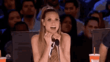 a woman is sitting in front of a microphone with her mouth open in front of a crowd of people .