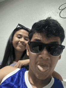 a man wearing sunglasses sticks out his tongue next to a girl