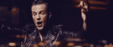 a man in a leather jacket is standing with his arms outstretched .