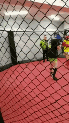 a man in a green jacket stands behind a chain link fence watching a boxer
