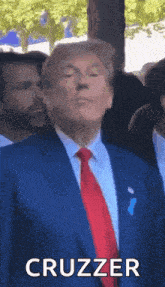 donald trump is wearing a blue suit and red tie and making a funny face while standing in front of a crowd .