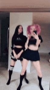 two girls are dancing in front of a mirror and one of them is taking a picture of herself .