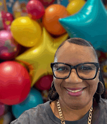 a woman wearing glasses is smiling in front of a bunch of balloons