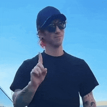 a man wearing sunglasses and a baseball cap is pointing his finger up .
