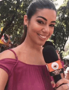 a woman in a pink off the shoulder top is holding a microphone and smiling