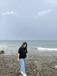 a woman is standing on a rocky beach looking at the ocean .