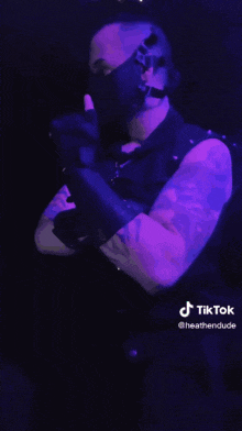 a man with a tattoo on his arm is wearing a mask and a purple light behind him