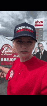 a woman wearing a hat and a red shirt is standing in front of a sign for a gas station .