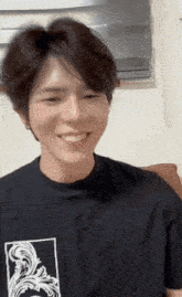 a young man wearing a black t-shirt with a picture of a woman on it smiles