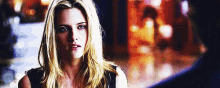 a woman with long blonde hair is looking at the camera with a blurry background