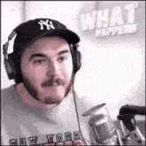 a man wearing headphones and a ny hat is standing in front of a microphone and a sign that says what happened