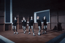 a group of women are dancing on a stage in front of a blackboard