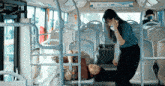 a woman talking on a cell phone while standing next to a man laying on a bus .