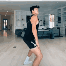 a man in a black tank top and shorts is standing in a living room .