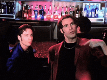 two men are standing in front of a bar with bottles on it