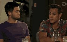 two men are sitting at a table and one is wearing a purple shirt with a polo logo