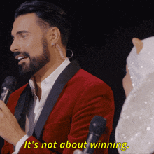 a man in a red suit says it 's not about winning while holding a microphone