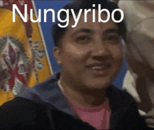 a man in a pink shirt is smiling in front of a flag that says ' nungyribo ' on it