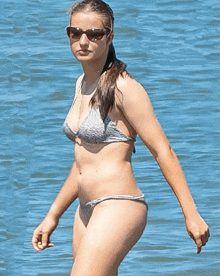 a woman in a bikini and sunglasses walking in the water