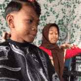 a boy is getting his hair cut by a woman wearing a brown hijab