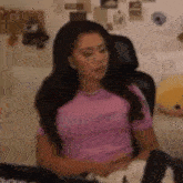 a woman in a pink shirt is sitting in a chair and talking on a cell phone .