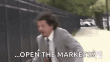a man in a suit and tie is running down a street and says `` open the markets '' .