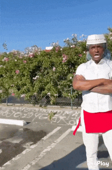 a man in a white shirt and red apron stands with his arms crossed
