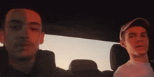 two men are sitting in a car and one has a red hat on