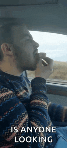 a man with a beard is sitting in a car eating a sandwich .