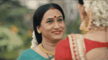 a woman in a blue sari is smiling at another woman in a red saree .