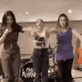 three women are dancing in front of a drum set that says the warning