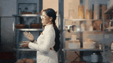a woman wearing glasses stands in front of a shelf with a drone flying in the background