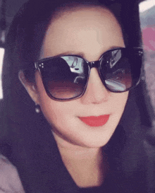 a woman wearing sunglasses and red lipstick smiles in a car