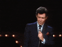 a man in a suit is singing into a microphone in a dark room .