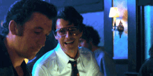 a man wearing glasses and a tie smiles while another man looks on