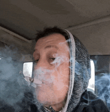 a man wearing a hooded jacket is smoking a pipe