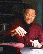 a man in a red jacket is sitting at a table with a top hat on it