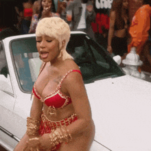a woman in a red bra and gold bracelets is standing in front of a white car