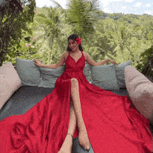 a woman in a red dress sits on a bed with pillows