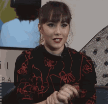 a woman wearing a black and red floral shirt with the word aitana on the bottom left