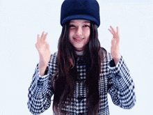 a woman wearing a blue hat and a plaid jacket is making a peace sign